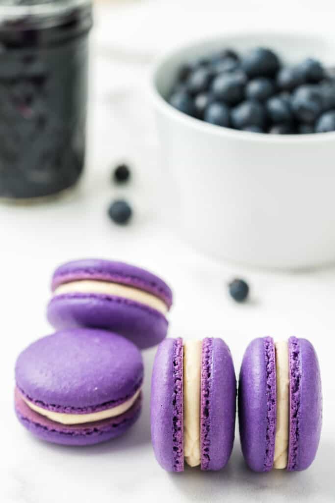 Blueberry macarons in a bowl on a wooden serving board.