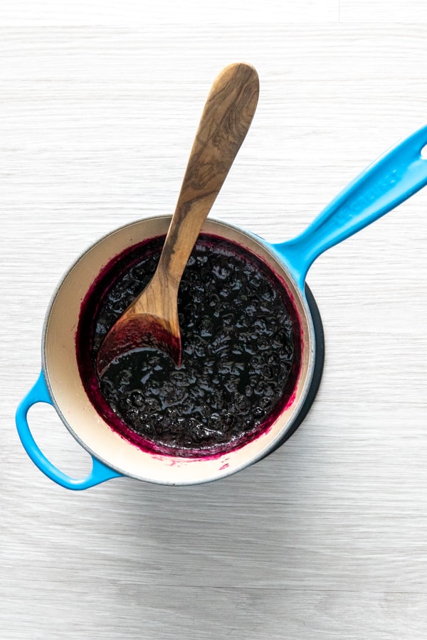 Blueberry jam with crushed blueberries and a wooden spoon in a saucepan.