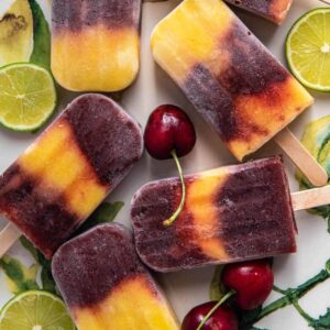 Cherry mango popsicles on a platter with fresh cherries and lime.