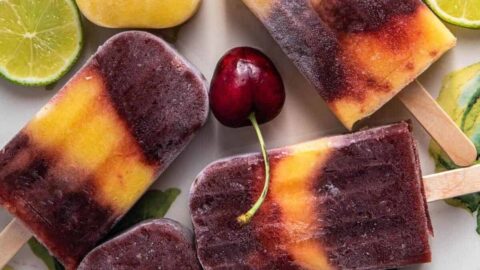 Cherry mango popsicles on a platter with fresh cherries and lime.