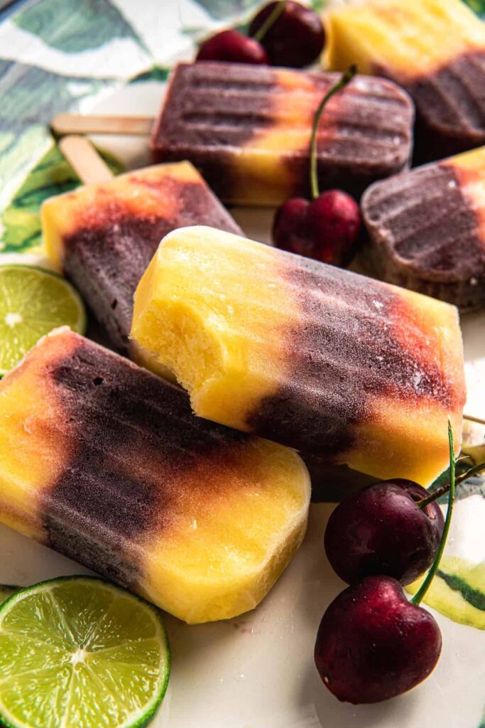 Cherry mango popsicles on a plate with limes.