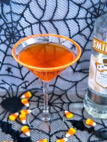 Candy corn cocktail next to a bottle of vodka with candy corn scattered around.