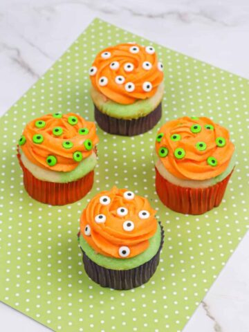 Four halloween monster eyeball cupcakes on a green napkin.