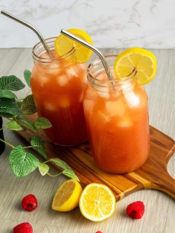 Two mason jars with iced guava black tea lemonade on a wooden serving board.