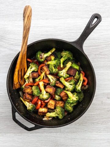 Mongolian tofu with vegetables in a cast iron skillet with wooden turner.