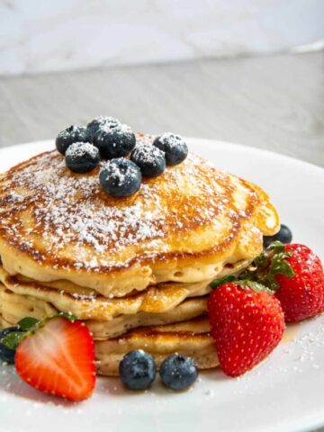 Pancakes made with evaporated milk on a white plate with strawberries, blueberries, and powdered sugar.