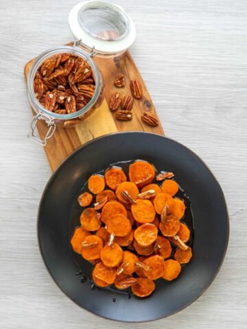 Stovetop candied sweet potatoes on a black plate and wooden serving board with pecans.