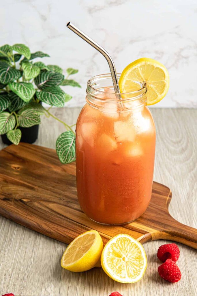 Iced guava black tea lemonade recipe on a wooden serving board with lemons and raspberries