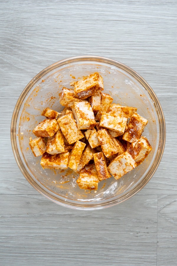Tofu in a glass bowl tossed in spices and cornstarch.