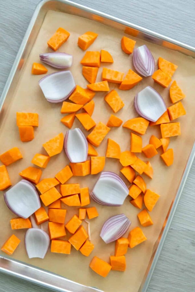 Sweet potatoes and red onion on a baking sheet.