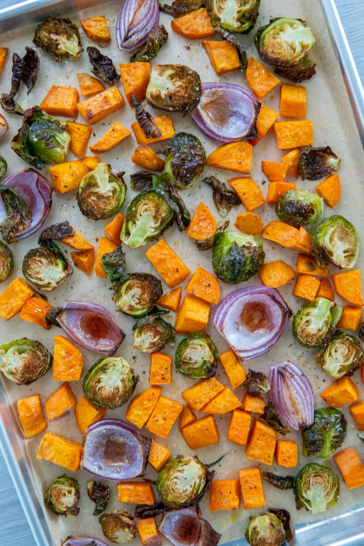Red onions, sweet potatoes, and brussel sprouts on a baking sheet.