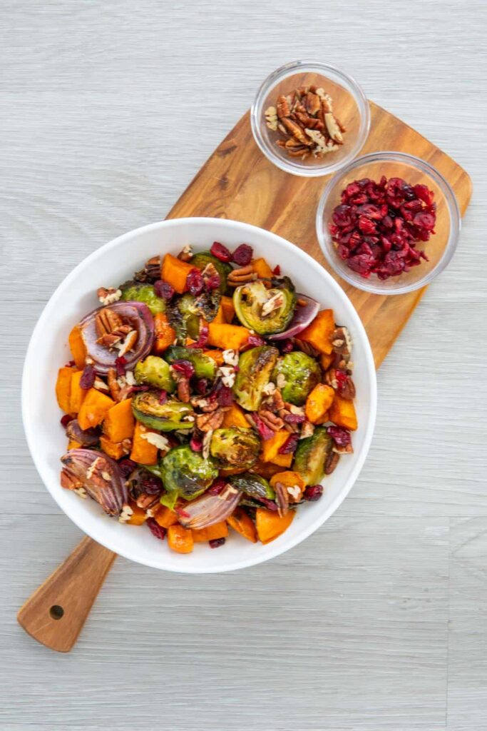 Roasted brussel sprouts sweet potatoes recipe served in a white bowl with dried cranberries and toasted pecans.