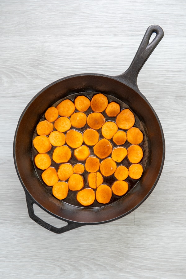 Sweet potatoes with sauce spooned on top in a cast iron pan.
