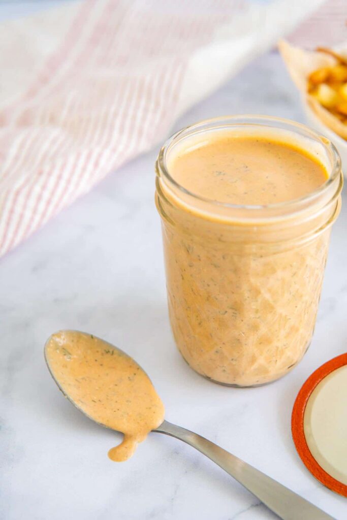 A jar of BBQ ranch dressing next to a spoon with dressing dripping off.