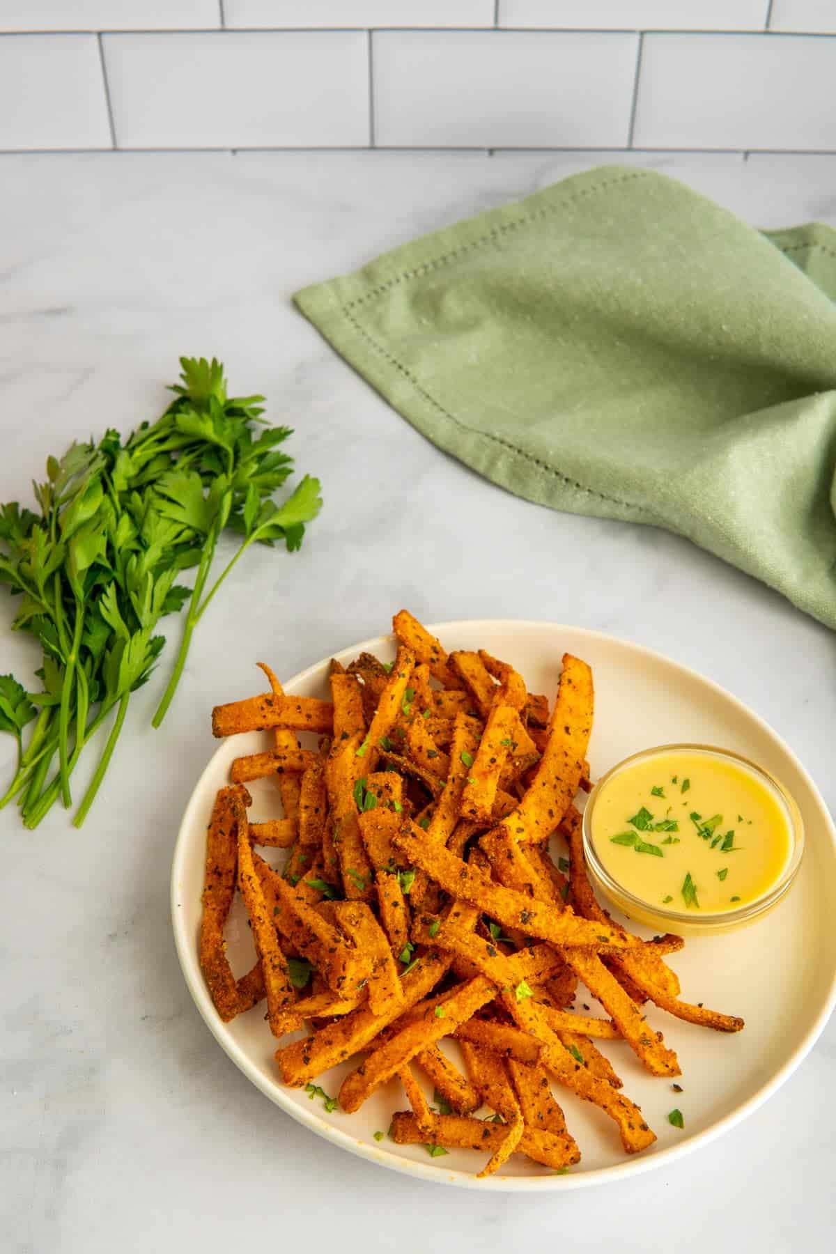 Air fryer butternut squash fries on a white plate with parsley and a green napkin.