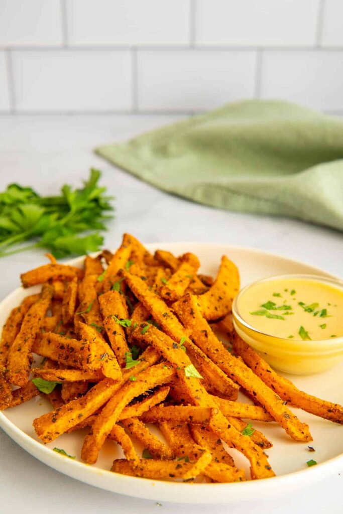 Air fryer butternut squash fries on a white plate with maple mustard sauce and a green napkin.