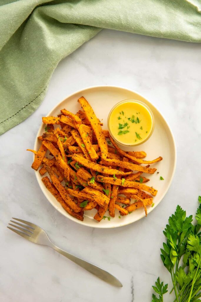 An overhead shot of air fryer butternut squash fries on a marble background with a form, parsley, and a green napkin.