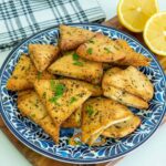 Air fryer pita chips on a blue plate with lemon and parsley.