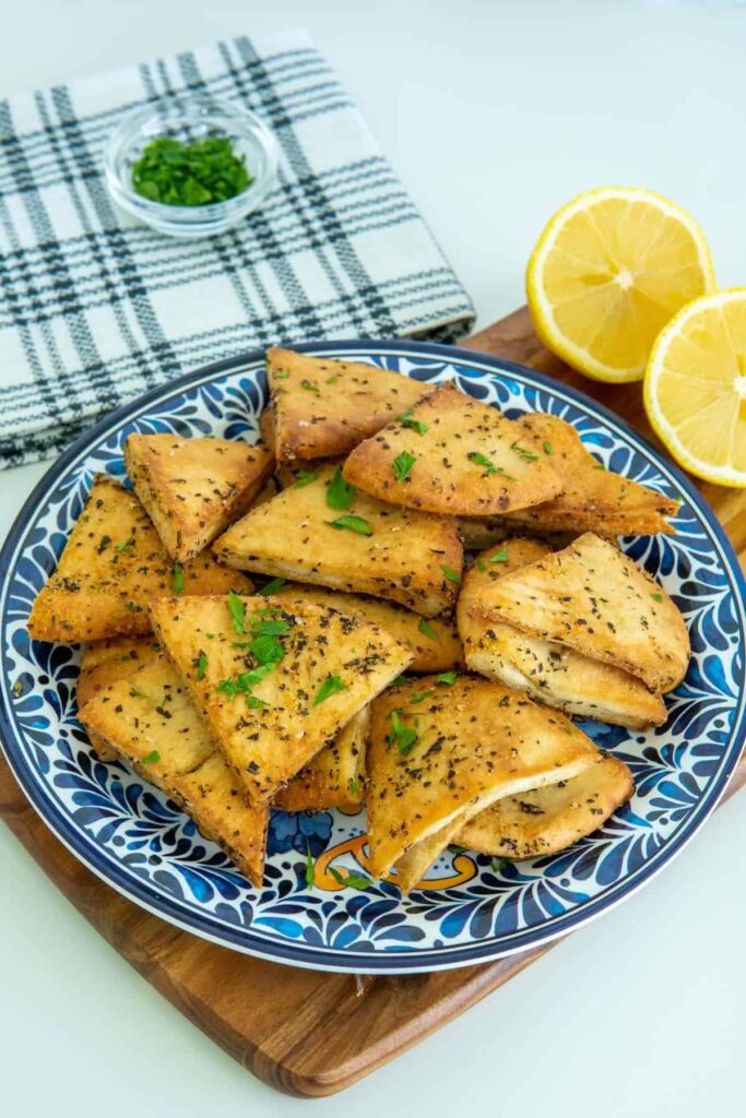 Air fryer pita chips on a blue plate with lemons.