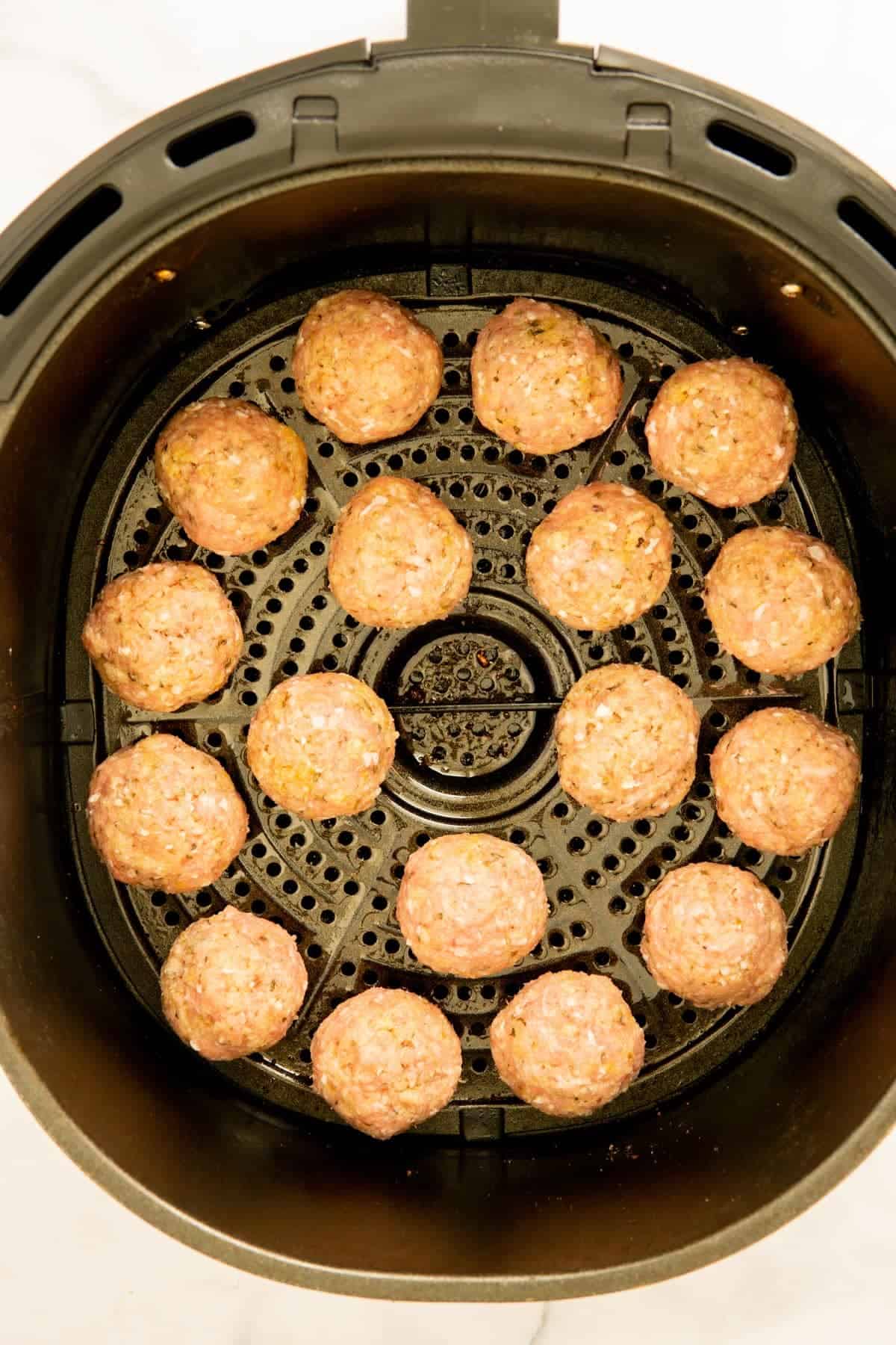Raw turkey meatballs in an air fryer basket.