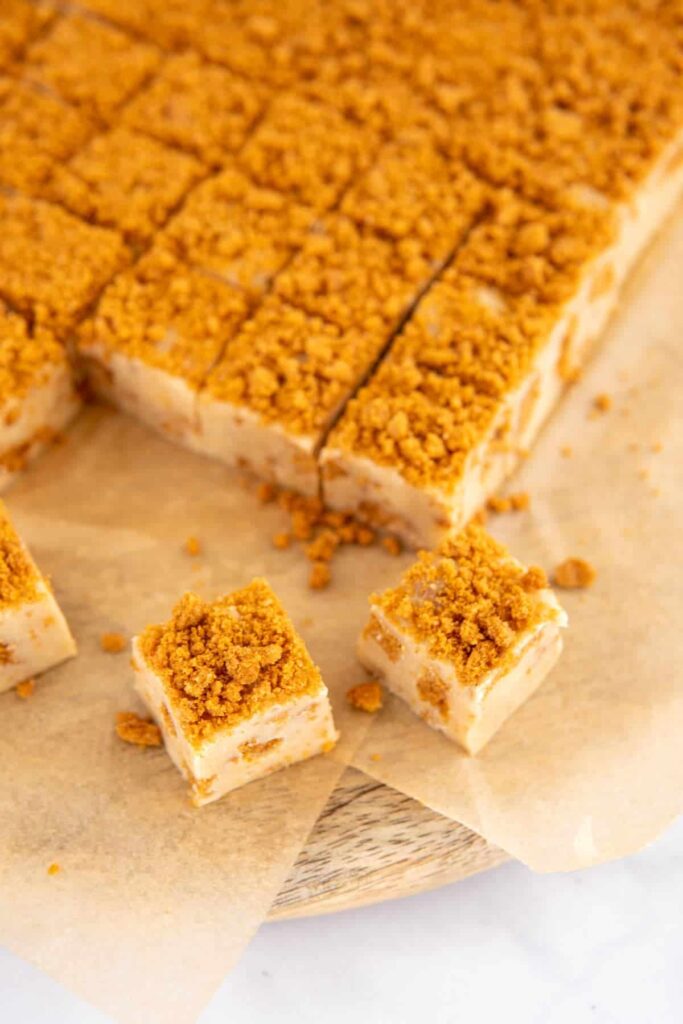 Biscuff fudge cut into squares on a wooden board and parchment.