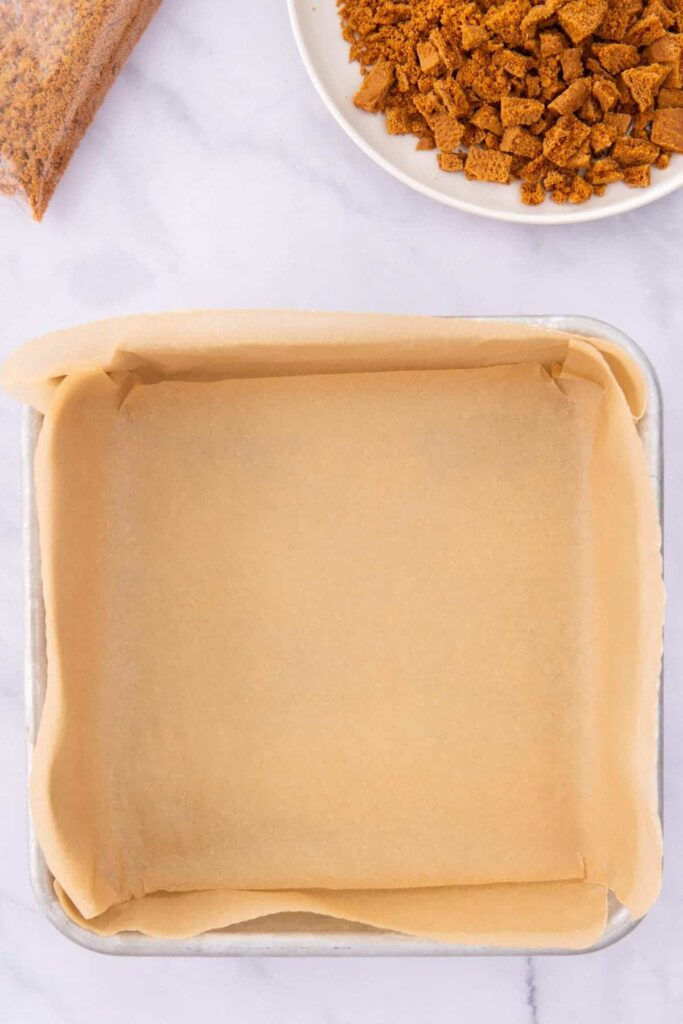 A square 8x8 inch pan lined with brown parchment paper.