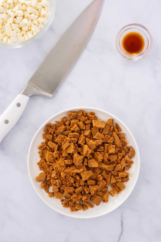 Roughly chopped biscoff cookies on a white plate with a knife.