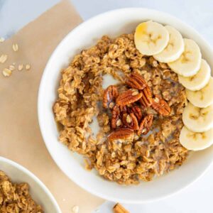 A bowl of cinnamon spice oatmeal on a square of parchment paper with oats scattered around.
