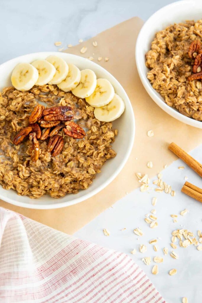 Two bowls of cinnamon spice oatmeal topped with pecans and bananas.