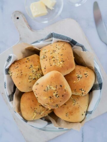 A bowl of air fryer dinner rolls next to a knife and a small bowl of butter.
