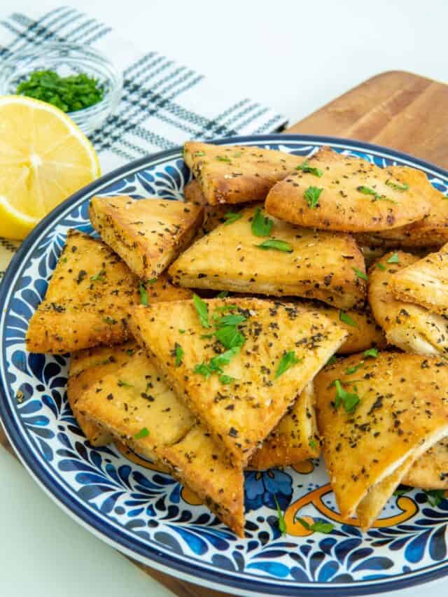 Air fryer pita chips on a blue plate with lemon and parsley.