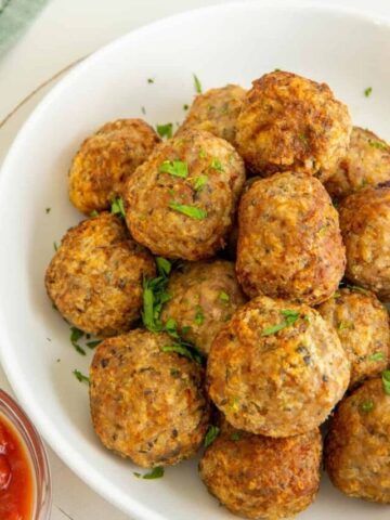 Air fryer turkey meatballs on a white plate with marinara sauce and a green napkin.