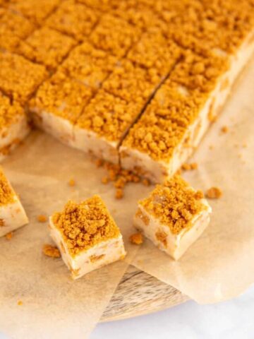 Biscuff fudge cut into squares on a wooden board and parchment.