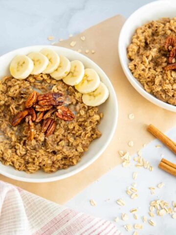 Two bowls of cinnamon spice oatmeal topped with pecans and bananas.