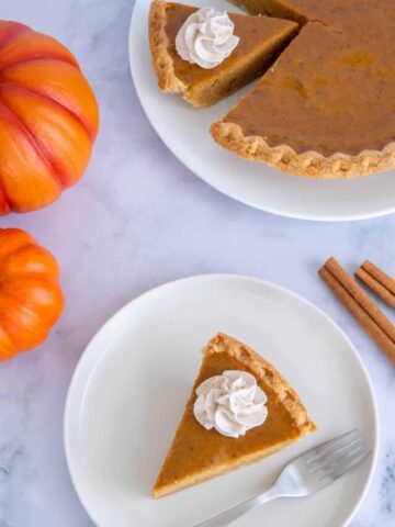 A slice of pumpkin pie next to a whole pie.