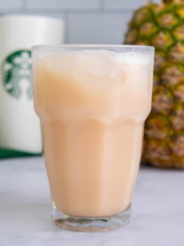 Guava passion fruit Starbucks recipe drink in a glass in front of a pineapple.