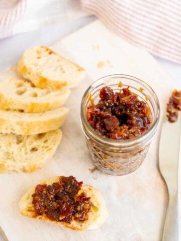 A jar of maple bacon onion jam next to a a slice of bread with jam.