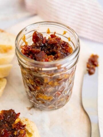 Maple bacon onion jam in a jar with a knife and a slice of bread with jam.