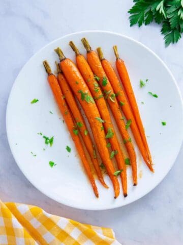Maple glazed carrots with brown sugar on a white plate with a yellow napkin.