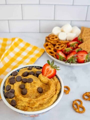 Pumpkin spice hummus in a bowl with a yellow plaid napkin and a plate of sweet sides.