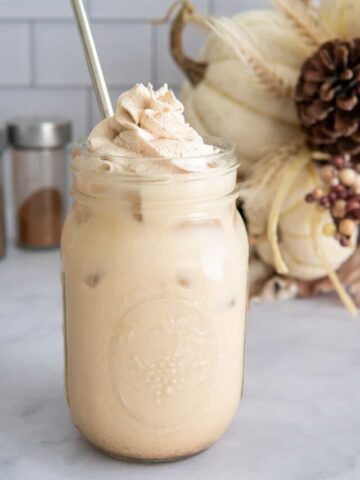 Pumpkin spice iced latte with whipped cream in a mason jar.