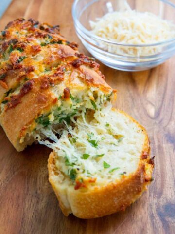 Parmesan stuffed garlic bread on a wooden board with a bowl of parmesan cheese.