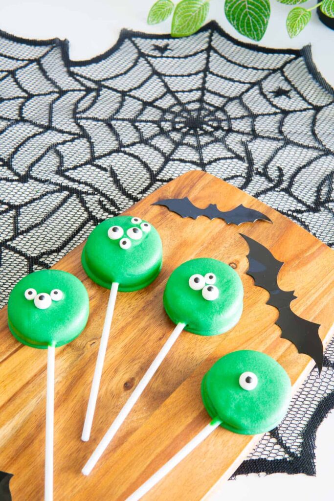 Halloween chocolate covered oreos on a wooden serving board with bats.