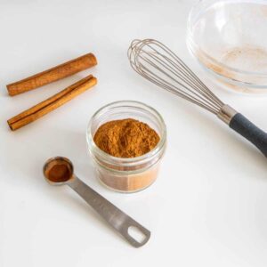 Homemade pumpkin pie spice mix in a glass jar with cinnamon sticks and allspice.