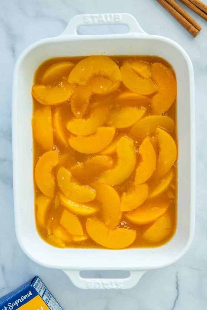 Peach cobbler filling in a white baking dish.