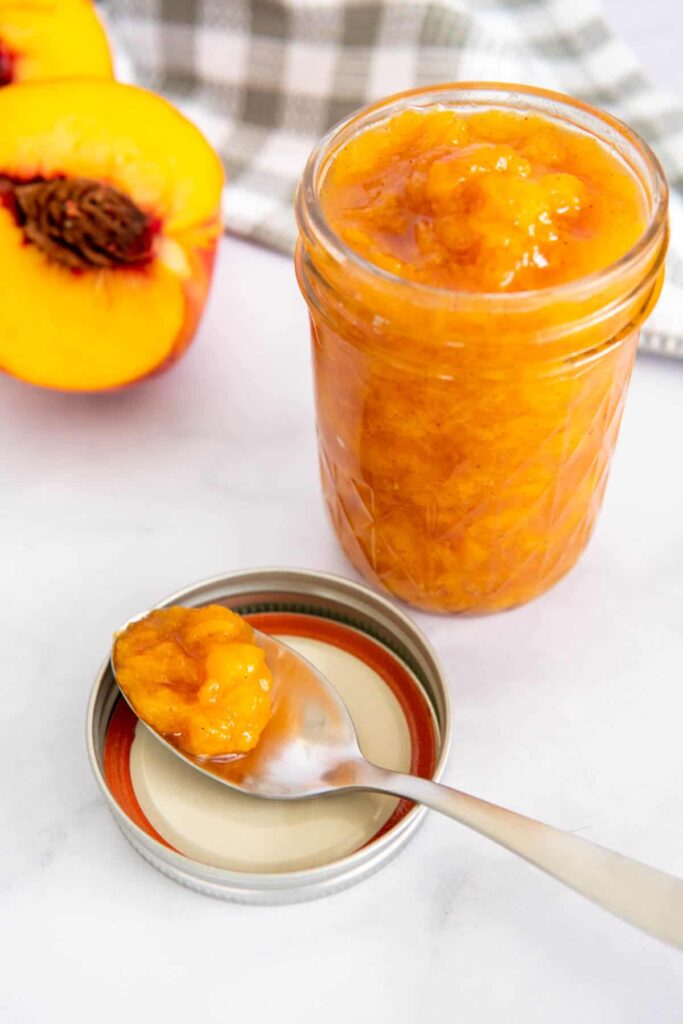 Peach jam on a spoon next to a jar of peach jam.