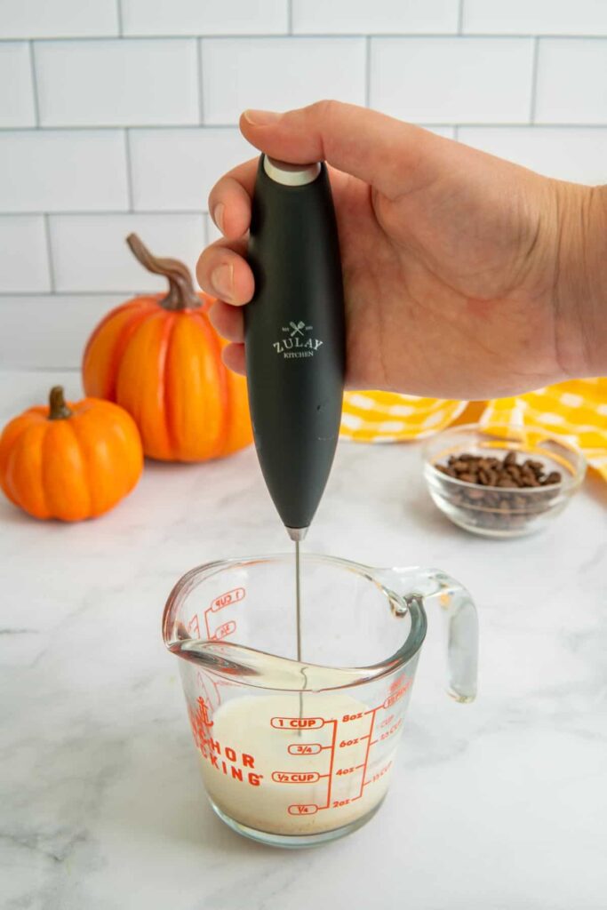 Milk being made into cold foam with a handheld electric milk frother.