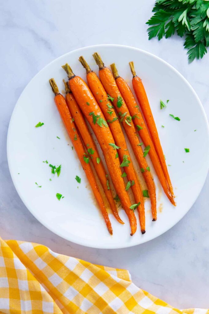 Maple glazed carrots with brown sugar on a white plate with a yellow napkin.