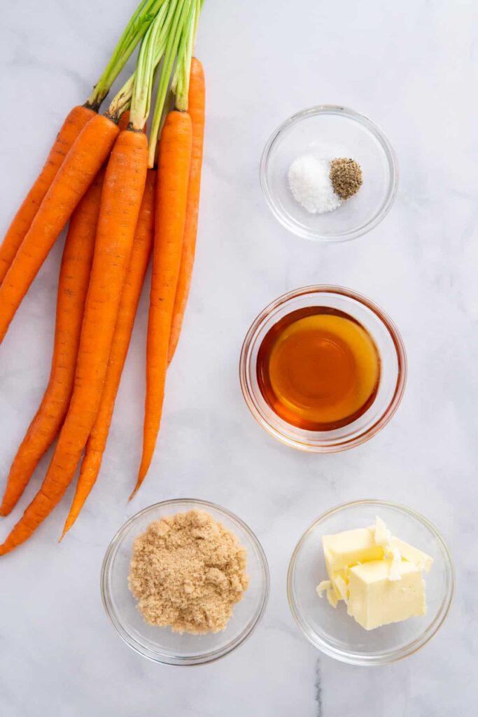 Ingredients for maple glazed carrots brown sugar on a white marble background.