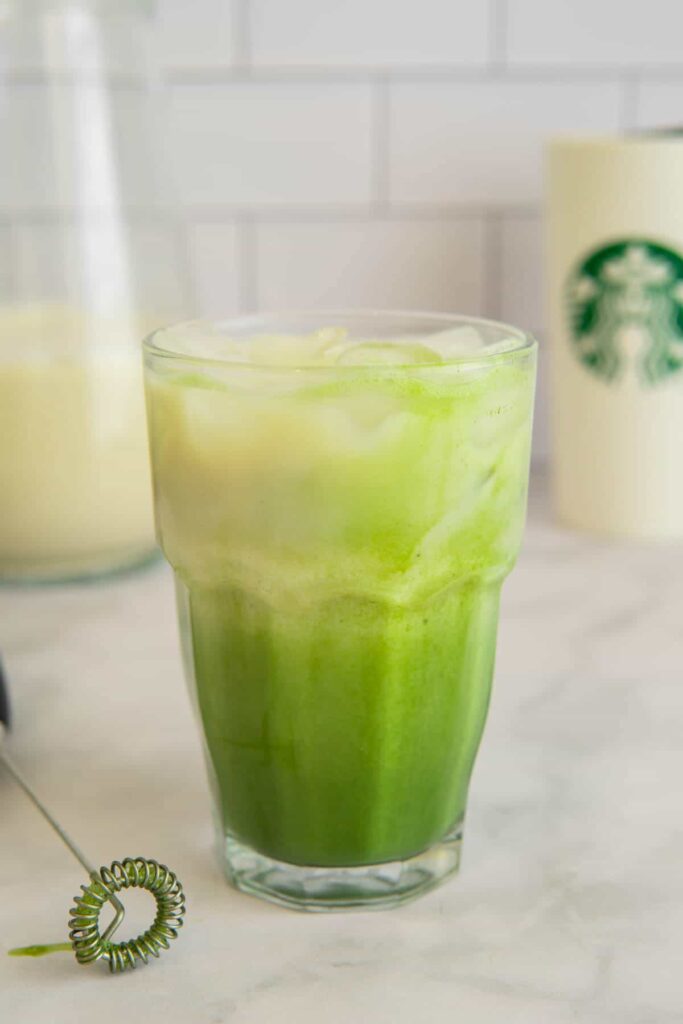 Oat milk matcha latte in a glass with a Starbucks cup in the background.
